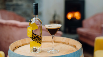 A bottle of our Cardi Bay Welsh Vodka and an Espresso Martini sitting on a barrel with a fire in the background.
