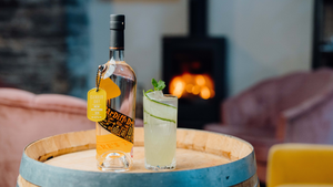 A bottle of our Cardiff Dry Welsh Gin and a Cucumber Southside sitting on a barrel with a fire in the background.