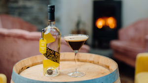 A bottle of our Cardi Bay Welsh Vodka and an Espresso Martini sitting on a barrel with a fire in the background.