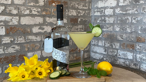 A bottle of our Dewi Sant Welsh Gin and a Garden Martini sitting on a barrel next to a bunch of daffodils.