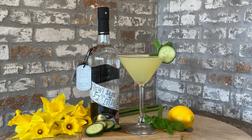 A bottle of our Dewi Sant Welsh Gin and a Garden Martini sitting on a barrel next to a bunch of daffodils.