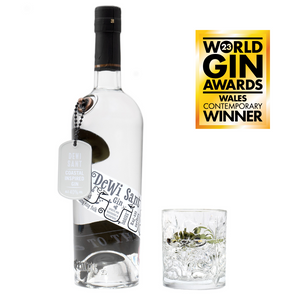 A 70cl bottle of Eccentric Spirit Co's Dewi Sant Welsh Gin alongside an old fashioned glass half-filled with the Welsh gin. A Gold Medal is displayed in the corner which was awarded to this Welsh gin at the World Gin Awards 2023.