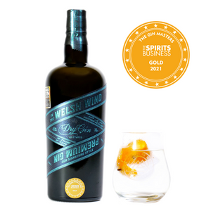A 70cl bottle of Signature Style Welsh Dry Gin by In The Welsh Wind Distillery alongside a glass of gin and tonic with an orange peel garnish. A Gold Medal is displayed in the corner which was awarded to this premium Welsh gin at the Gin Masters 2021.