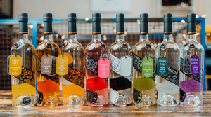 Each bottle in the Eccentric Spirit Co range of Welsh gin, Welsh rum and Welsh vodka standing side by side on a wooden table with some fairy lights in the background.