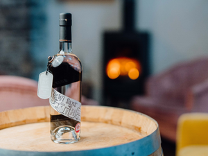 Our popular and Gold award-winning Dewi Sant Welsh Gin stood on a barrel with a fire burning in the background.