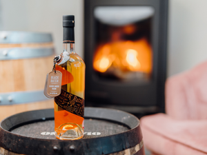 Our award-winning Black Batch Welsh Spiced Rum stood on a barrel with a fire burning in the background.